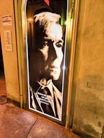 A portrait with a vintage aesthetic featuring a serious-looking individual in formal attire. The monochrome style with high contrast emphasizes the facial features and gives a dramatic tone. An Italian quote by Boris Pasternak is displayed at the bottom. The image is mounted on a door illuminated by a halo of light.