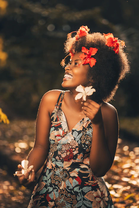 A joyful woman in a flowing ethnic dress, standing in a sunlit garden.