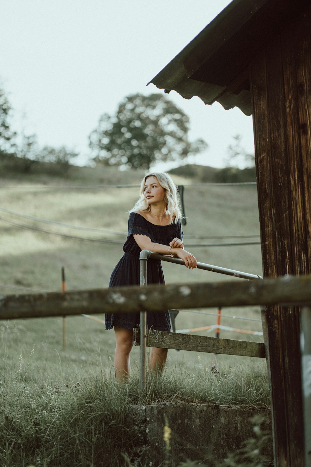 a woman in a black dress leaning on a fence