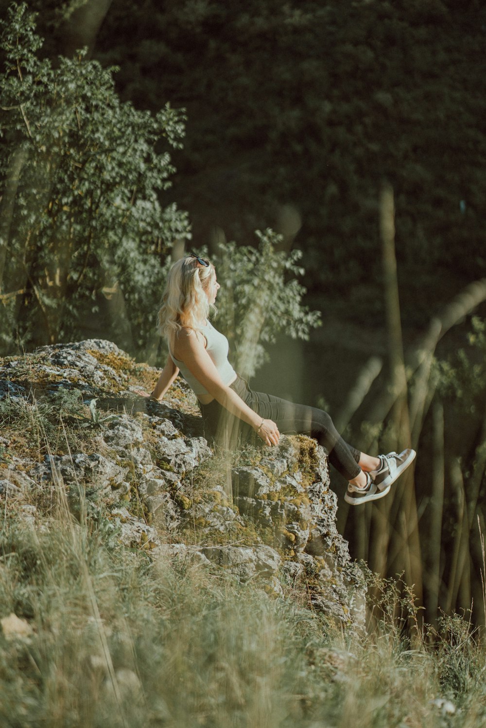 a woman sitting on top of a rock next to a forest