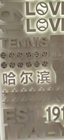 The image features a layered, three-dimensional display with words and symbols related to tennis. The words 'LOVE,' 'TENNIS,' and 'EST 1911 ITALY' are prominently featured. Symbols such as tennis balls and a racquet are included. There are also Chinese characters and plus signs, all designed in a monochromatic style with a lit background.