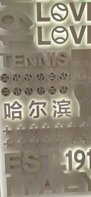 The image features a layered, three-dimensional display with words and symbols related to tennis. The words 'LOVE,' 'TENNIS,' and 'EST 1911 ITALY' are prominently featured. Symbols such as tennis balls and a racquet are included. There are also Chinese characters and plus signs, all designed in a monochromatic style with a lit background.
