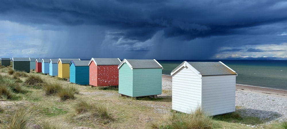 a row of beach huts sitting on top of a grass covered beach