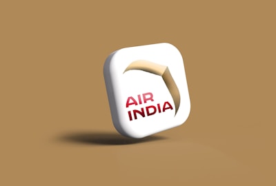 A stylized 3D icon featuring a white square with rounded edges. The icon has the text 'AIR INDIA' in red letters. Above the text, there is a design resembling a stylized arch or ribbon in shades of beige and brown.