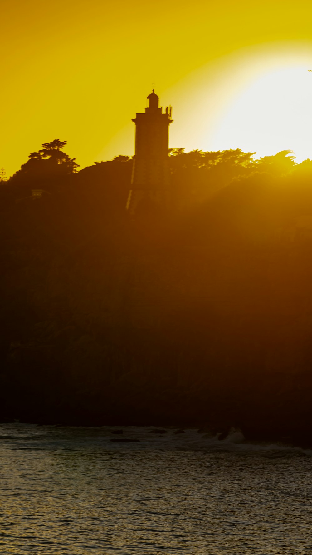 the sun is setting over the water with a lighthouse in the distance