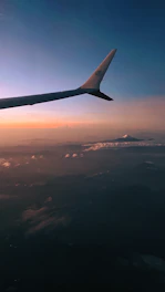 Wide aerial view of a virtual airplane soaring above mountains at sunset.
