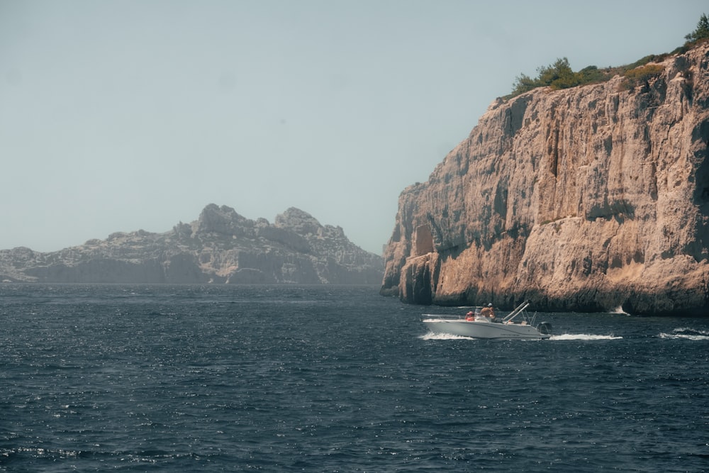 a boat traveling past a rocky cliff on the ocean