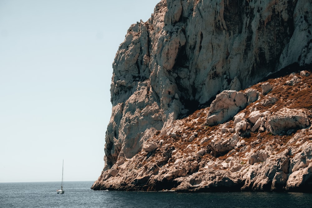 a sailboat in the water near a rocky cliff