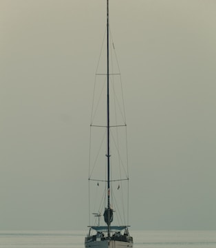 A minimalist composition of a lone sailboat on calm blue waters.