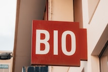 A red sign with the white letters 'BIO' mounted on a wall. The sign appears to be part of a storefront or business facade, surrounded by beige-colored walls.