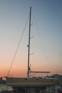 A sleek trimaran boat with retractable mast sails, solar panels, and wheels, docked peacefully by a serene coastline at sunset.