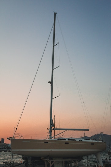 A sleek trimaran boat with retractable mast sails, solar panels, and wheels, docked peacefully by a serene coastline at sunset.
