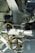 Close-up view of a metal mechanical component, likely part of an aircraft's landing gear assembly, featuring various wires, bolts, and a round light fixture. The image is filled with metallic textures and a mix of smooth and structured surfaces.