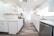 A modern, bright kitchen with white cabinetry and marble countertops. The room features stainless steel appliances, including a dishwasher and a stove, and has a wooden floor. Recessed lighting is installed in the ceiling, and natural light comes in through a large window with blinds.
