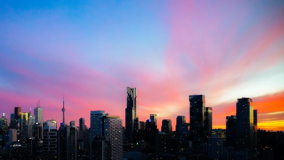 A vibrant city skyline at sunset with purple and orange hues reflecting the brand colors.