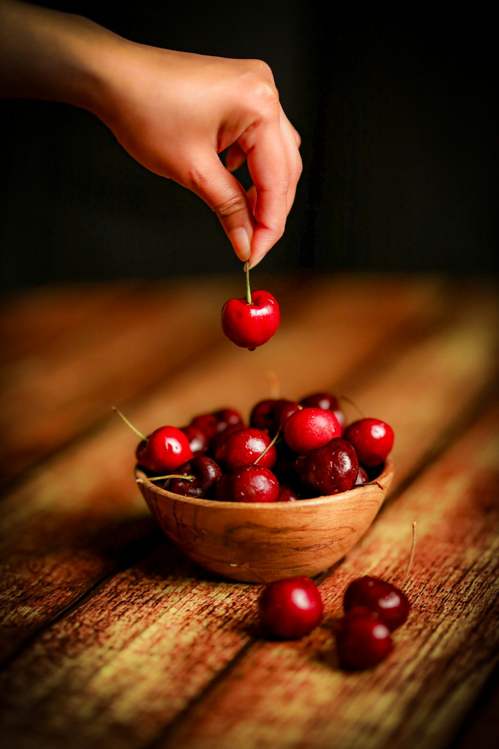 a person picking cherries from a wooden bowl