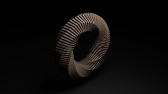 A three-dimensional twisted torus shape constructed from a series of uniform, rectangular sections, creating a spiraling pattern. The object is centered against a dark background, highlighting its geometric precision and textured surface.
