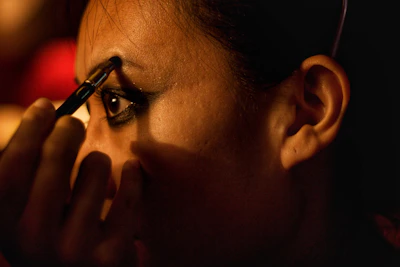 Side profile of a woman applying delicate, wispy Elise false eyelashes in soft lighting.