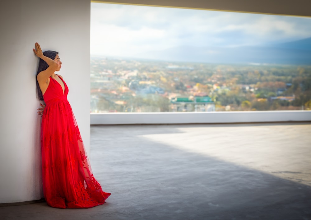 a woman in a red dress leaning against a wall
