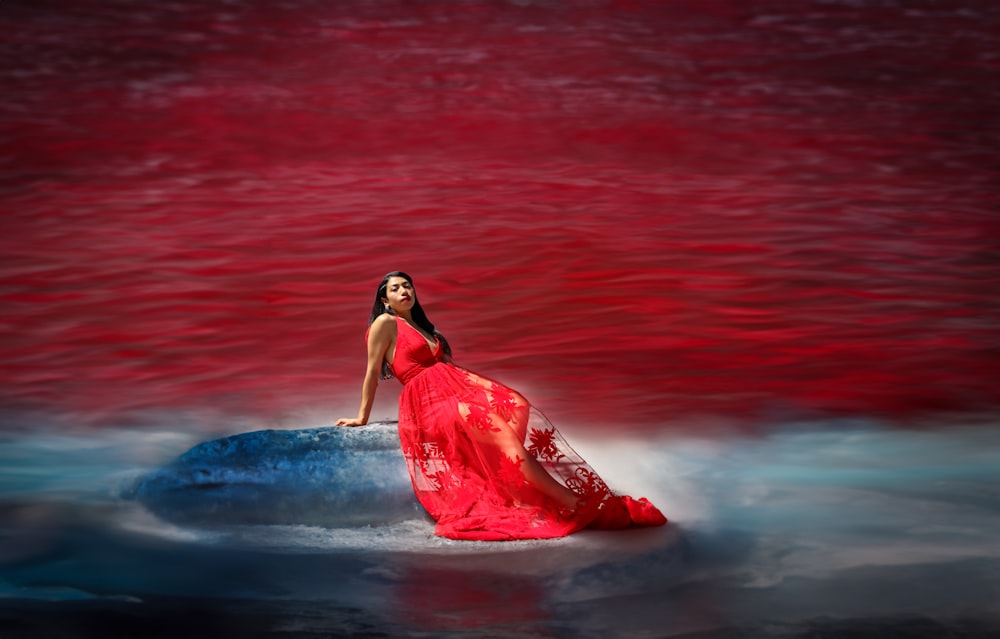 a woman in a red dress sitting on a rock