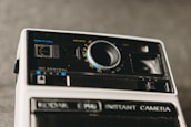 A vintage Kodak instant camera is prominently featured, showcasing its lens and various control knobs against a blurred background. The camera has a classic design with black and white elements, and the brand name is visibly printed.