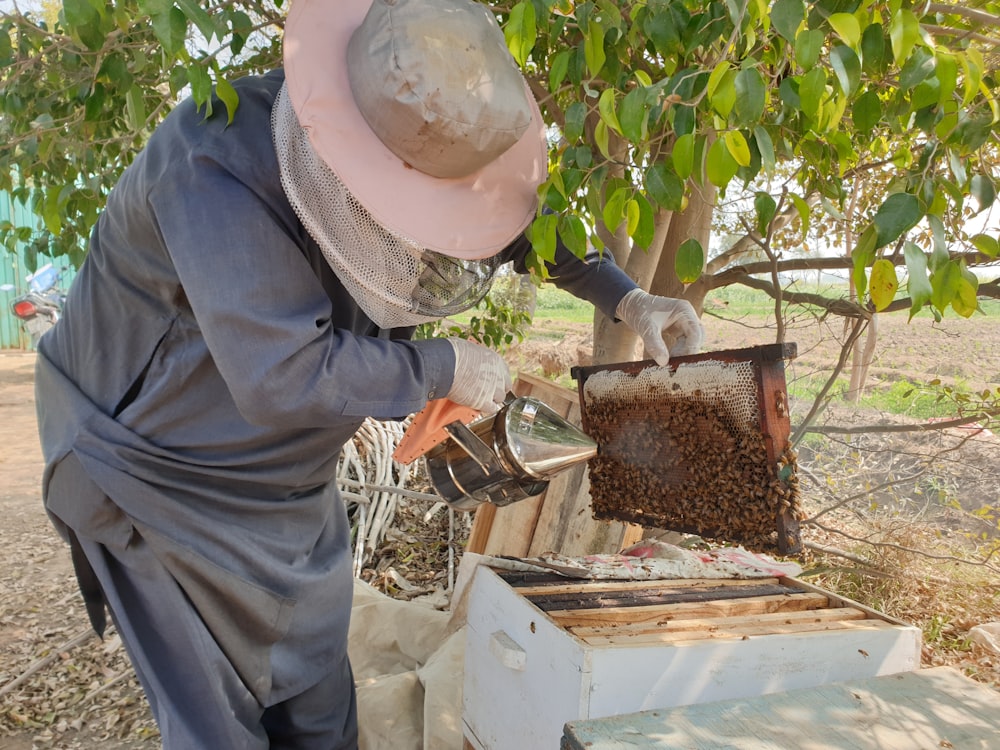 a man in a bee suit and hat inspecting a beehive