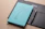 Close-up of a hand holding a sleek Fisher’s Creek notebook with turquoise accents on a clean white desk.