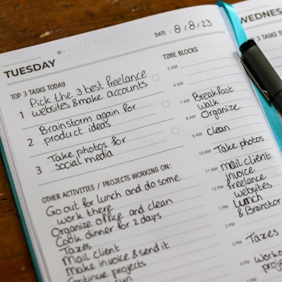 A planner page for Tuesday features a to-do list with tasks such as 'Pick the 3 best freelance websites', 'Brainstorm for product ideas', and 'Take photos for social media'. Below, there are additional activities and a schedule with time blocks. A pen rests on the page, and the date 8/8/23 is visible at the top.