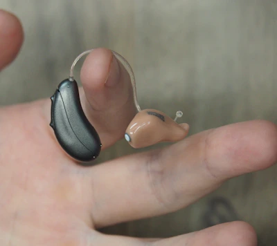 Hands of a technician adjusting a modern hearing aid under bright workshop lights.