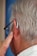 An elderly person with grey hair uses a hearing aid. The person is wearing glasses and has their finger touching the hearing aid behind their ear.