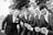 A diverse group of men smiling and wearing casual and formal outfits outdoors.
