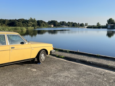 A serene landscape with a vintage car parked by a lake.