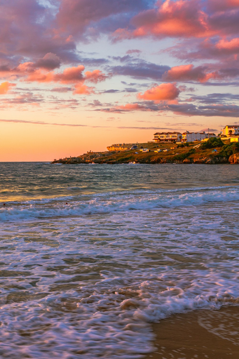 a beach with waves coming in to shore and houses in the distance