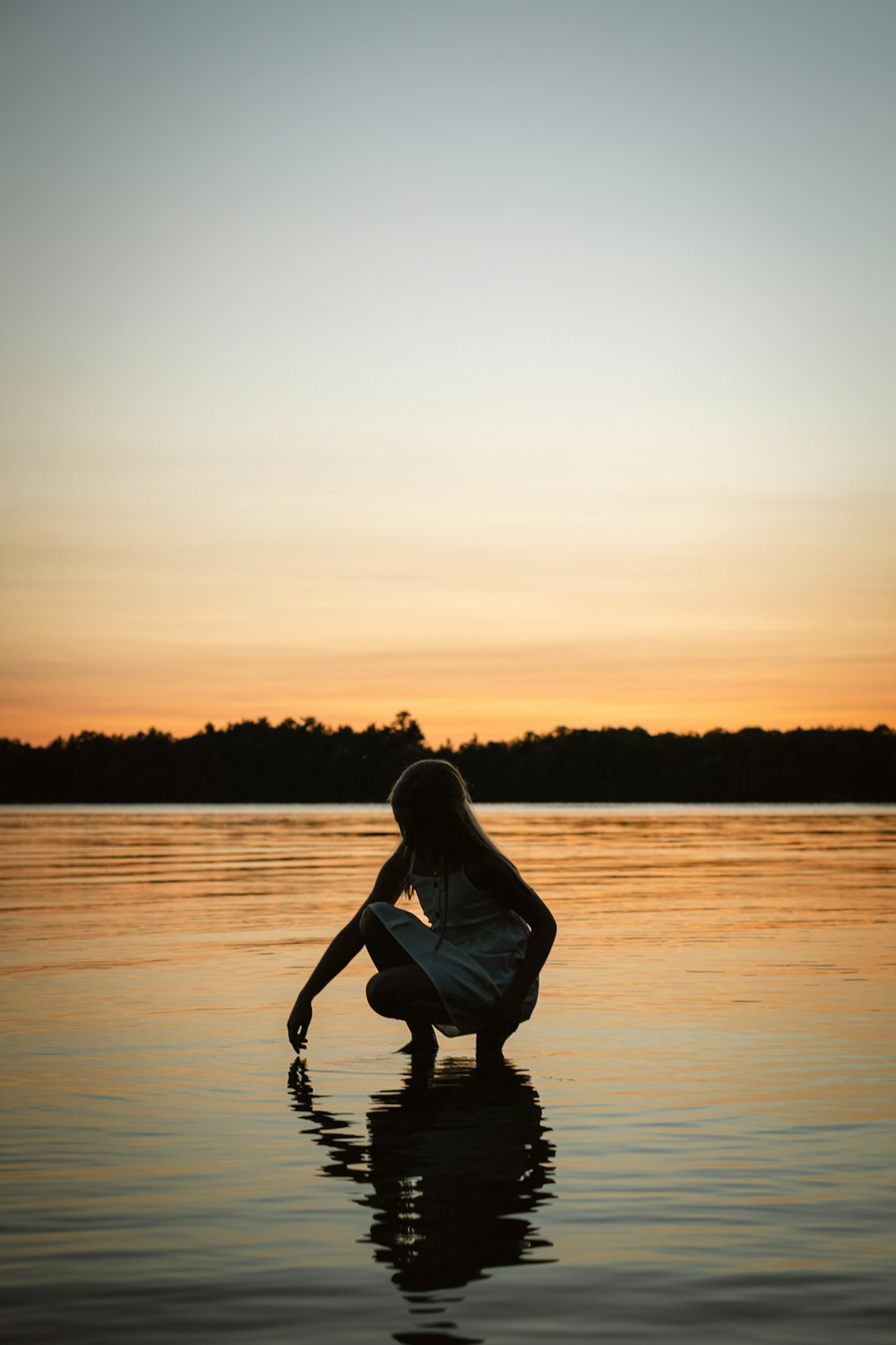 a woman kneeling down in the water at sunset