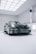 A sleek, luxury sports car with a glossy black finish is positioned in a modern, well-lit showroom. The car features distinctive curves and aerodynamic design, emphasizing its high-performance capabilities. The environment is minimalistic, with white walls and ceiling lights creating a clean and futuristic ambiance.