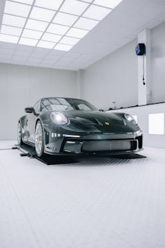 A sleek, luxury sports car with a glossy black finish is positioned in a modern, well-lit showroom. The car features distinctive curves and aerodynamic design, emphasizing its high-performance capabilities. The environment is minimalistic, with white walls and ceiling lights creating a clean and futuristic ambiance.