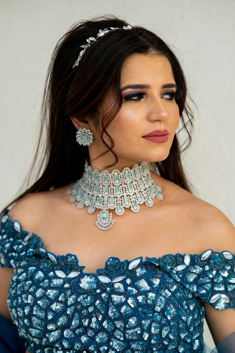 a woman in a blue dress with a necklace and earrings