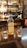 A bottle of Ballechin Highland Single Malt Scotch Whisky, aged 15 years, is placed on a wooden bar counter. Two glasses containing whisky are positioned next to the bottle. In the background, there is a wide variety of liquor bottles on shelves behind the bar, alongside a chalkboard with menu items. The setting is warmly lit, creating a cozy atmosphere.