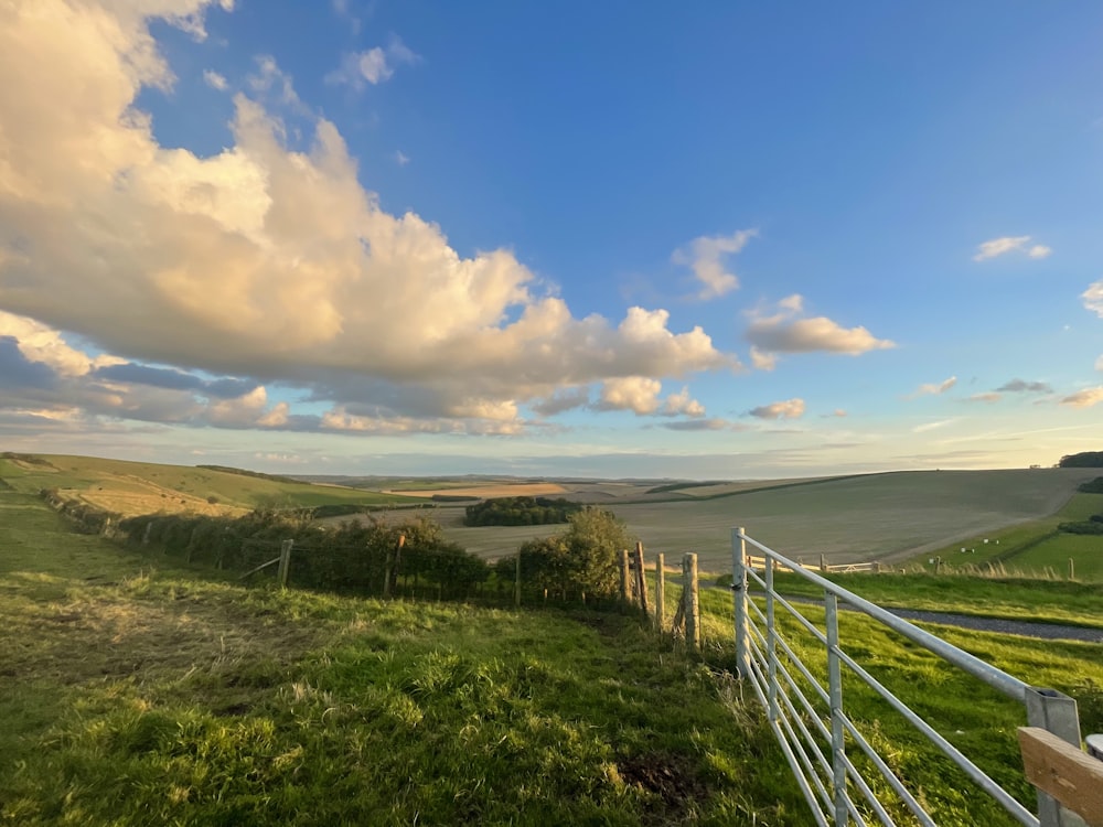 a white fence in a grassy field with rolling hills in the distance