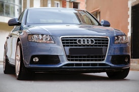 A sleek blue car with a prominent front grille and distinctive headlights. The shiny exterior and urban background suggest a modern, stylish setting.