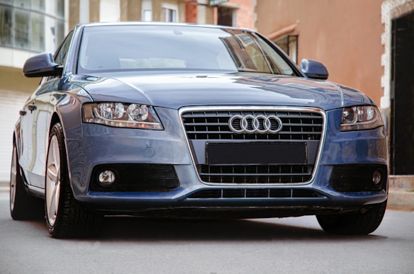 A sleek blue car with a prominent front grille and distinctive headlights. The shiny exterior and urban background suggest a modern, stylish setting.