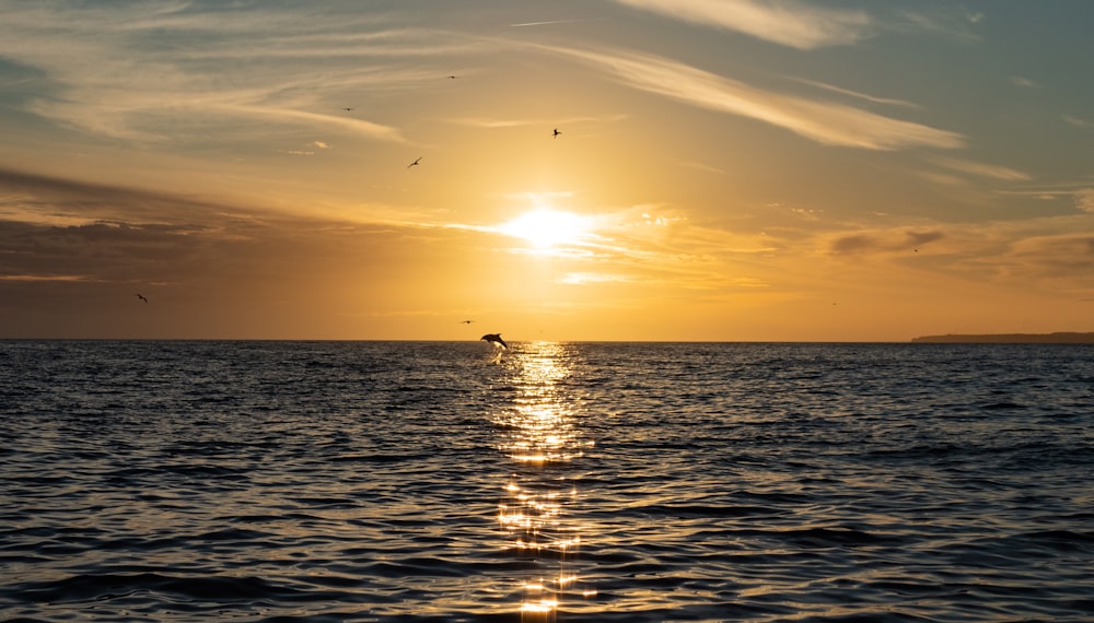 the sun is setting over the ocean with a boat in the distance