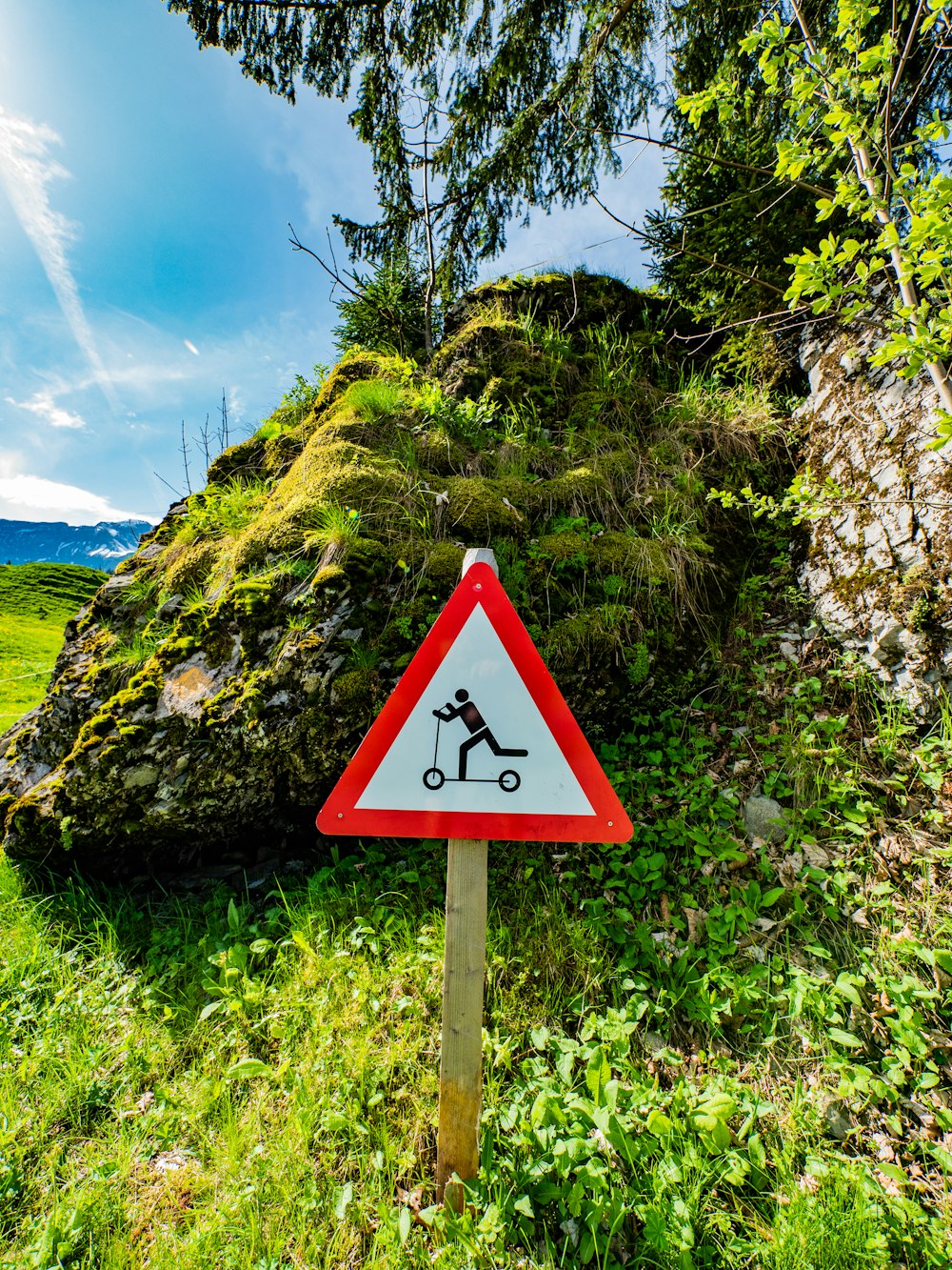 a red and white sign sitting on the side of a lush green hillside