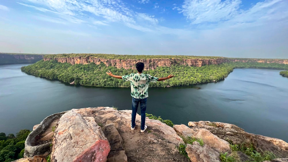 a man standing on top of a cliff overlooking a lake