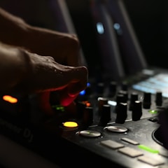 Hands adjusting a DJ mixer with glowing buttons and sliders.
