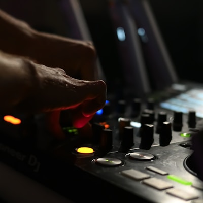Close-up of DJ hands adjusting mixer knobs with neon lights in background.