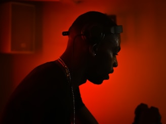 A silhouette of a person wearing headphones against a vibrant red background. The ambient lighting creates a dramatic and focused atmosphere, with the person seemingly engaged in music or audio-related activity.