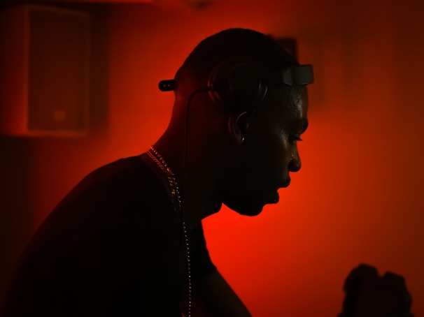 A silhouette of a person wearing headphones against a vibrant red background. The ambient lighting creates a dramatic and focused atmosphere, with the person seemingly engaged in music or audio-related activity.