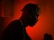 A silhouette of a person wearing headphones against a vibrant red background. The ambient lighting creates a dramatic and focused atmosphere, with the person seemingly engaged in music or audio-related activity.
