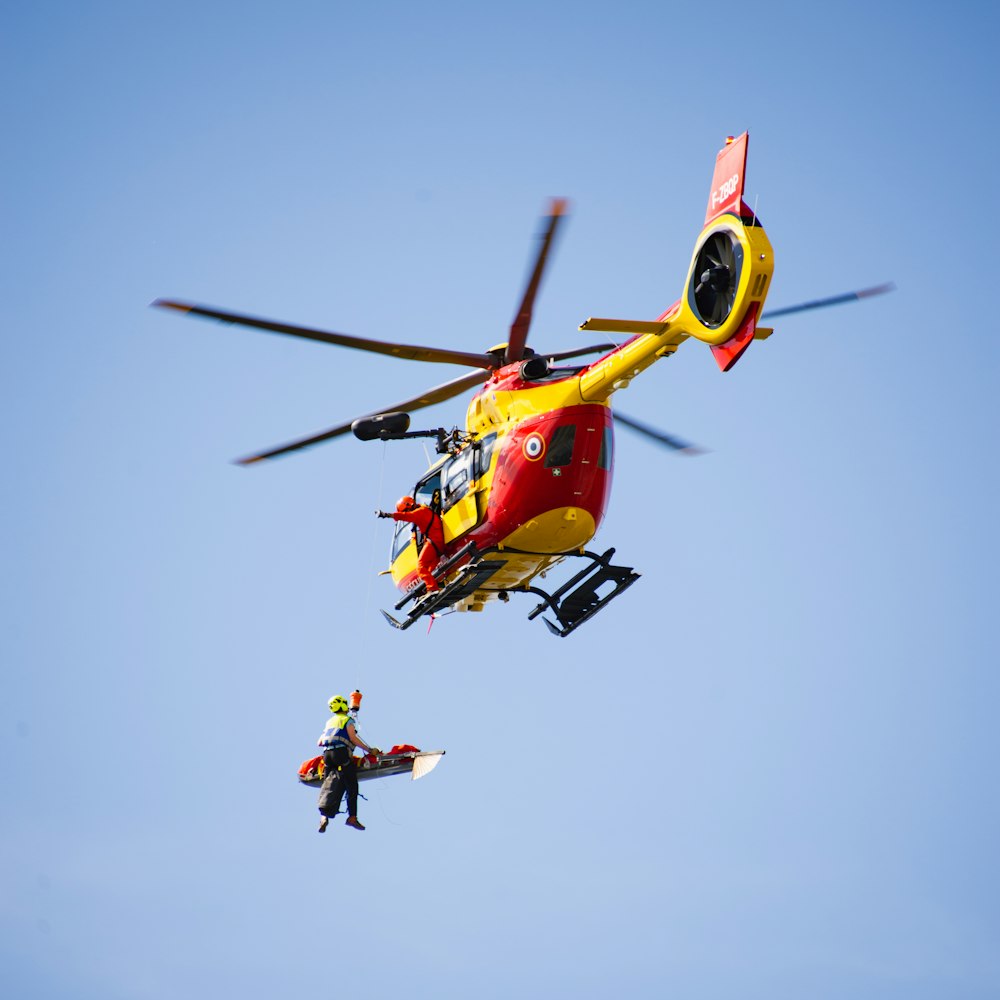 a red and yellow helicopter flying through a blue sky